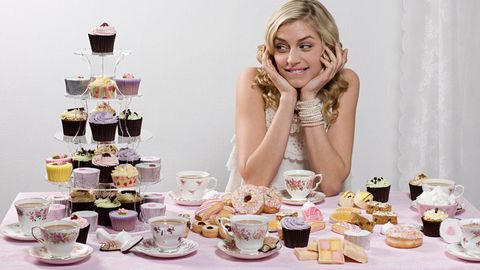 Woman at a table surrounded by cupcakes and other desserts